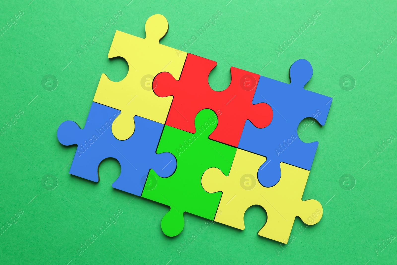 Image of Many colorful puzzle pieces on green background, top view. Symbol of autism