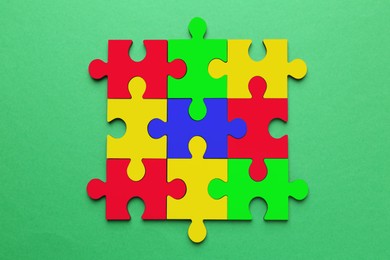 Image of Many colorful puzzle pieces on green background, top view. Symbol of autism