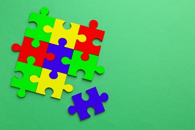 Many colorful puzzle pieces on green background, top view. Symbol of autism