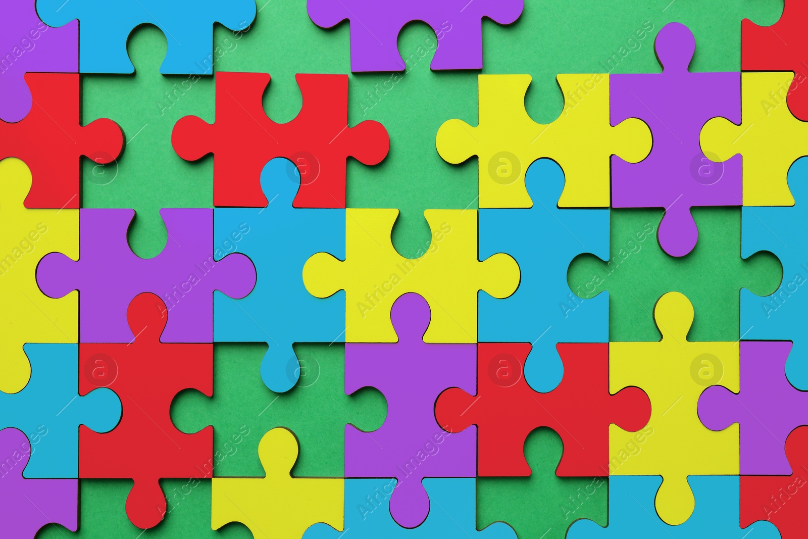 Image of Many colorful puzzle pieces on green background, top view. Symbol of autism