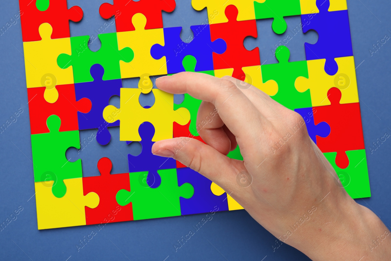 Image of Woman holding puzzle piece on blue background, top view. Autism concept