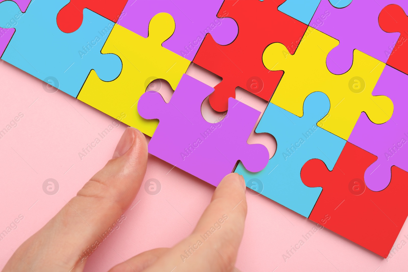 Image of Woman holding puzzle piece on pink background, top view. Autism concept