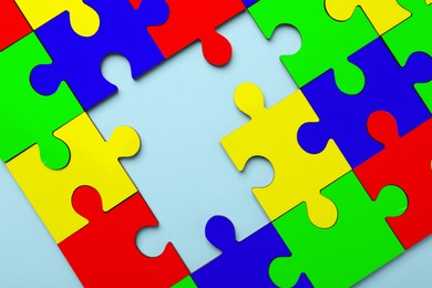 Many colorful puzzle pieces on light blue background, top view. Symbol of autism