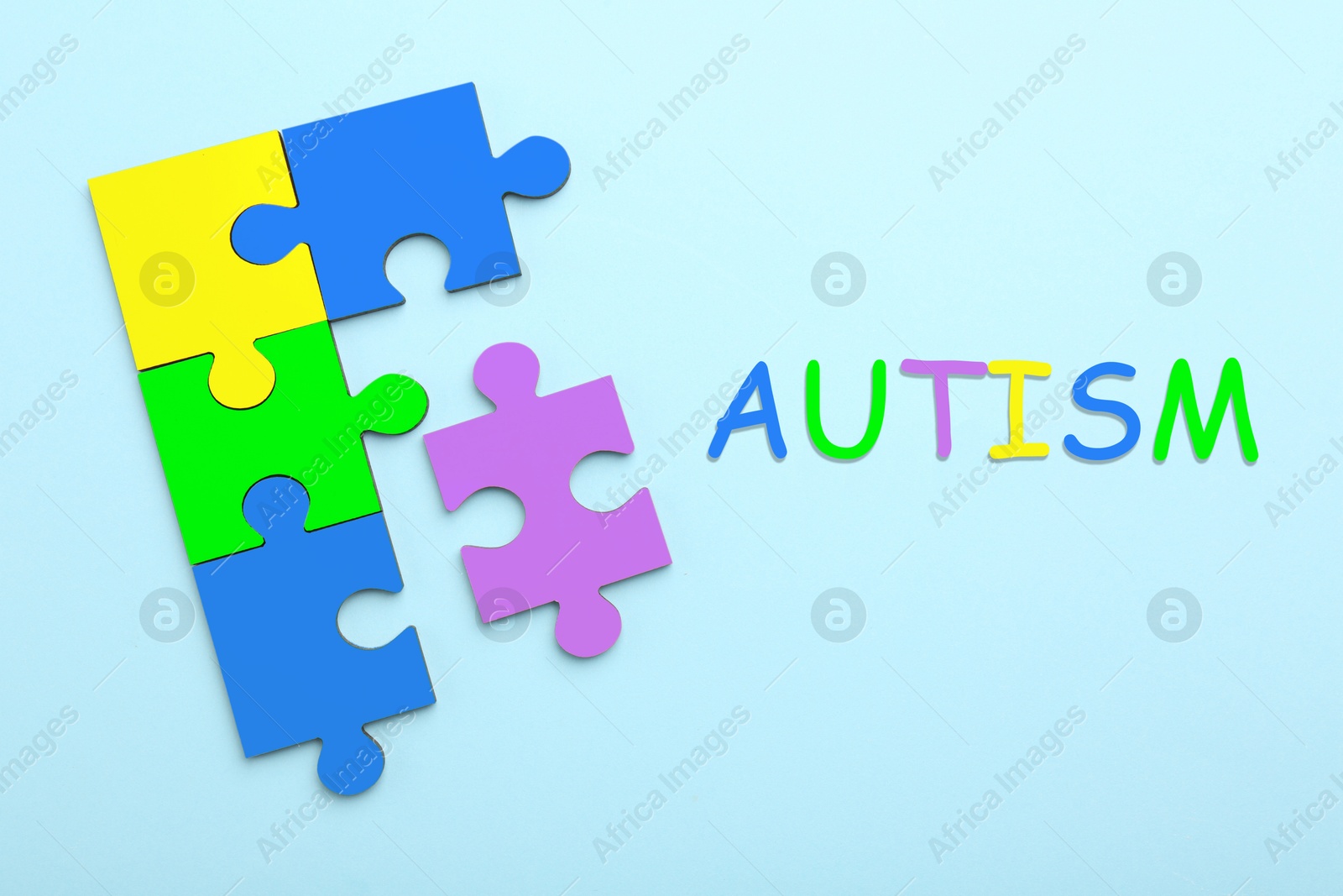 Image of Autism word and colorful puzzle pieces on light blue background, top view