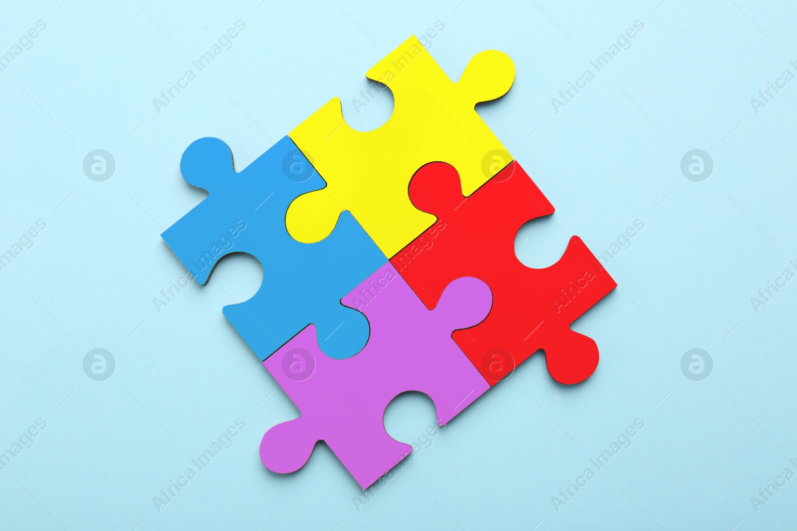 Image of Four colorful puzzle pieces on light blue background, top view. Symbol of autism