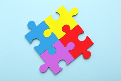 Image of Four colorful puzzle pieces on light blue background, top view. Symbol of autism