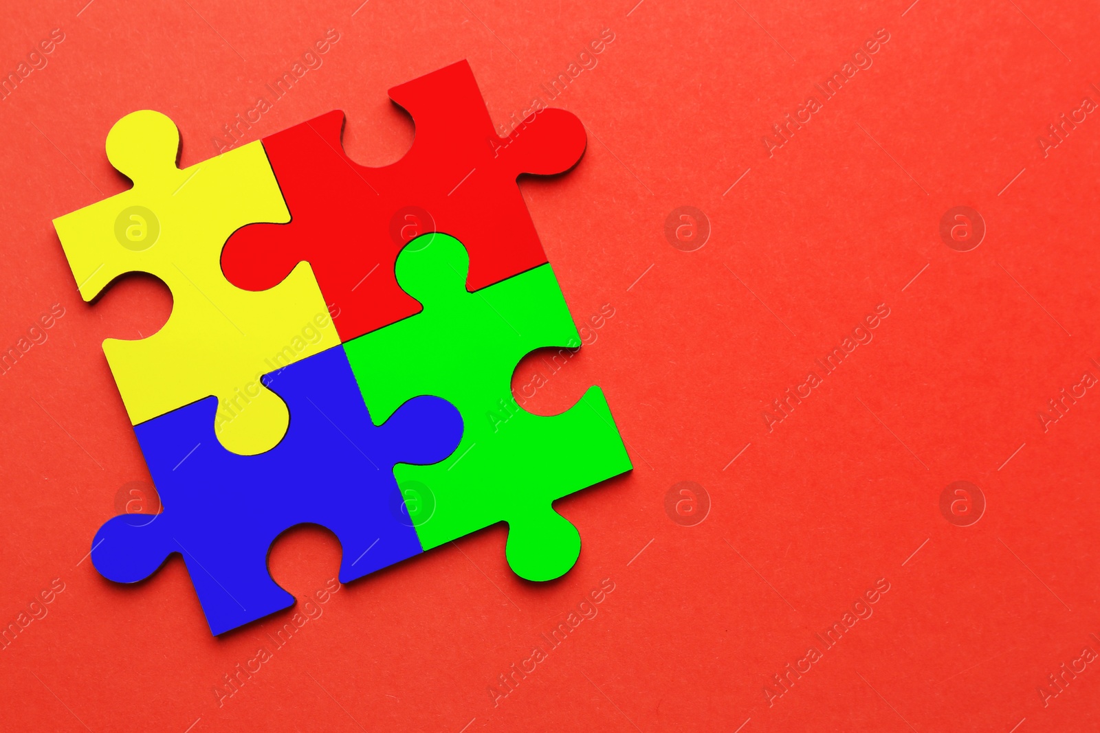 Image of Four colorful puzzle pieces on red background, top view. Symbol of autism