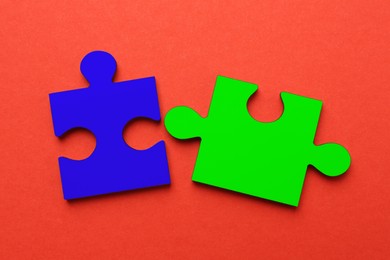 Image of Two colorful puzzle pieces on red background, top view. Symbol of autism