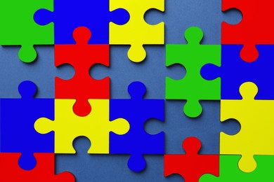 Image of Many colorful puzzle pieces on blue background, top view. Symbol of autism