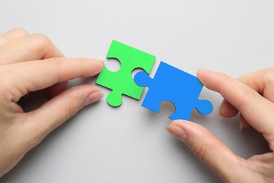 Image of Woman joining puzzle pieces on light grey background, top view. Autism concept