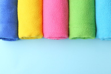 Rolled different microfiber cloths on light blue background, top view