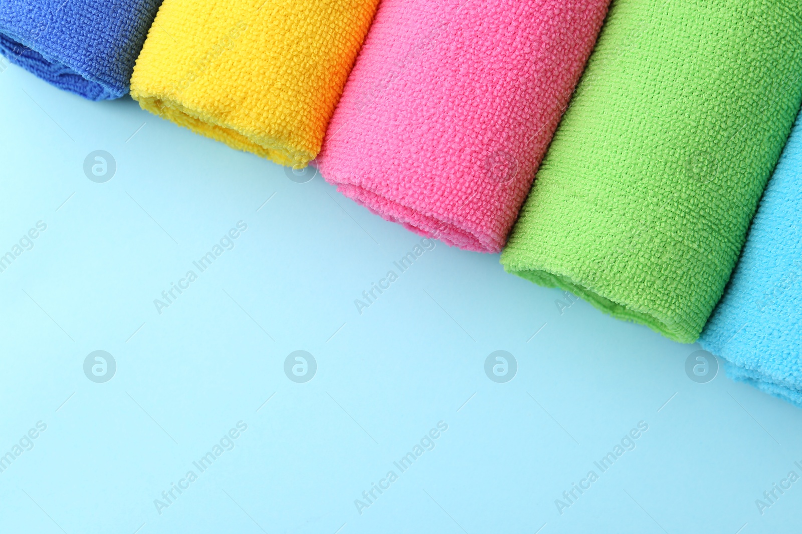 Photo of Rolled different microfiber cloths on light blue background, top view. Space for text