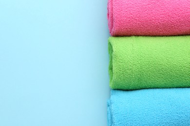 Photo of Rolled different microfiber cloths on light blue background, top view. Space for text