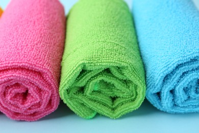 Rolled different microfiber cloths on light blue background, closeup