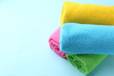 Photo of Rolled different microfiber cloths on light blue background, closeup. Space for text