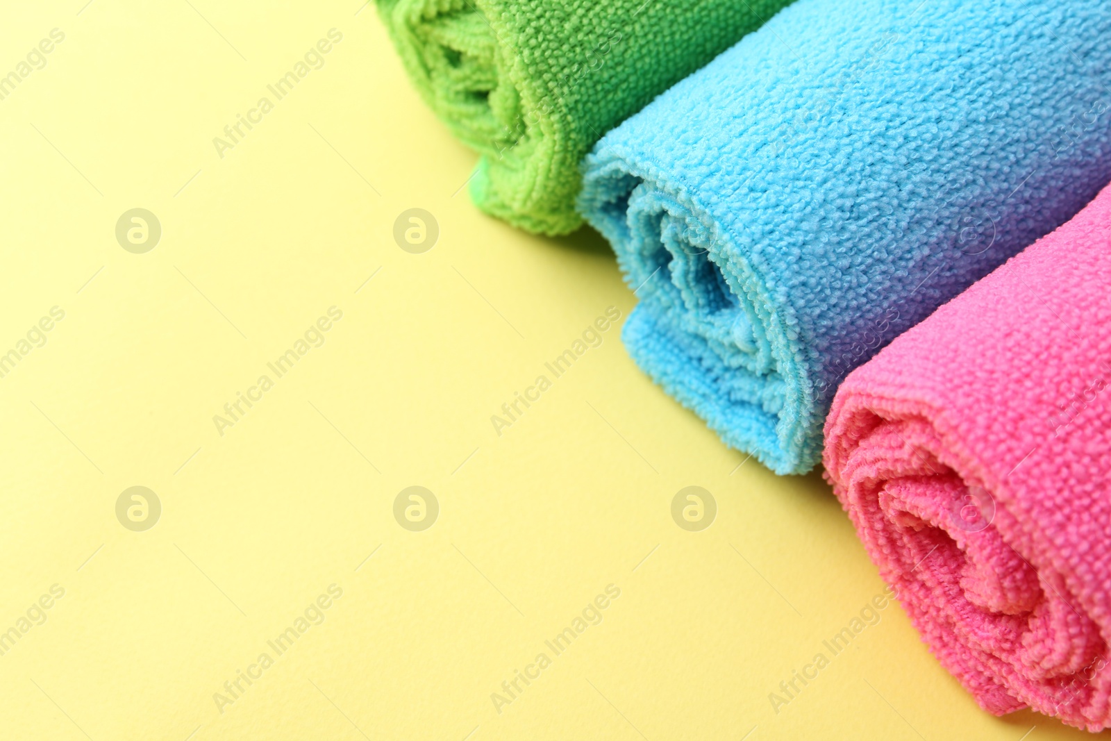 Photo of Rolled different microfiber cloths on yellow background, closeup. Space for text