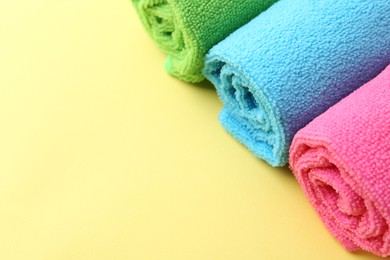 Rolled different microfiber cloths on yellow background, closeup. Space for text