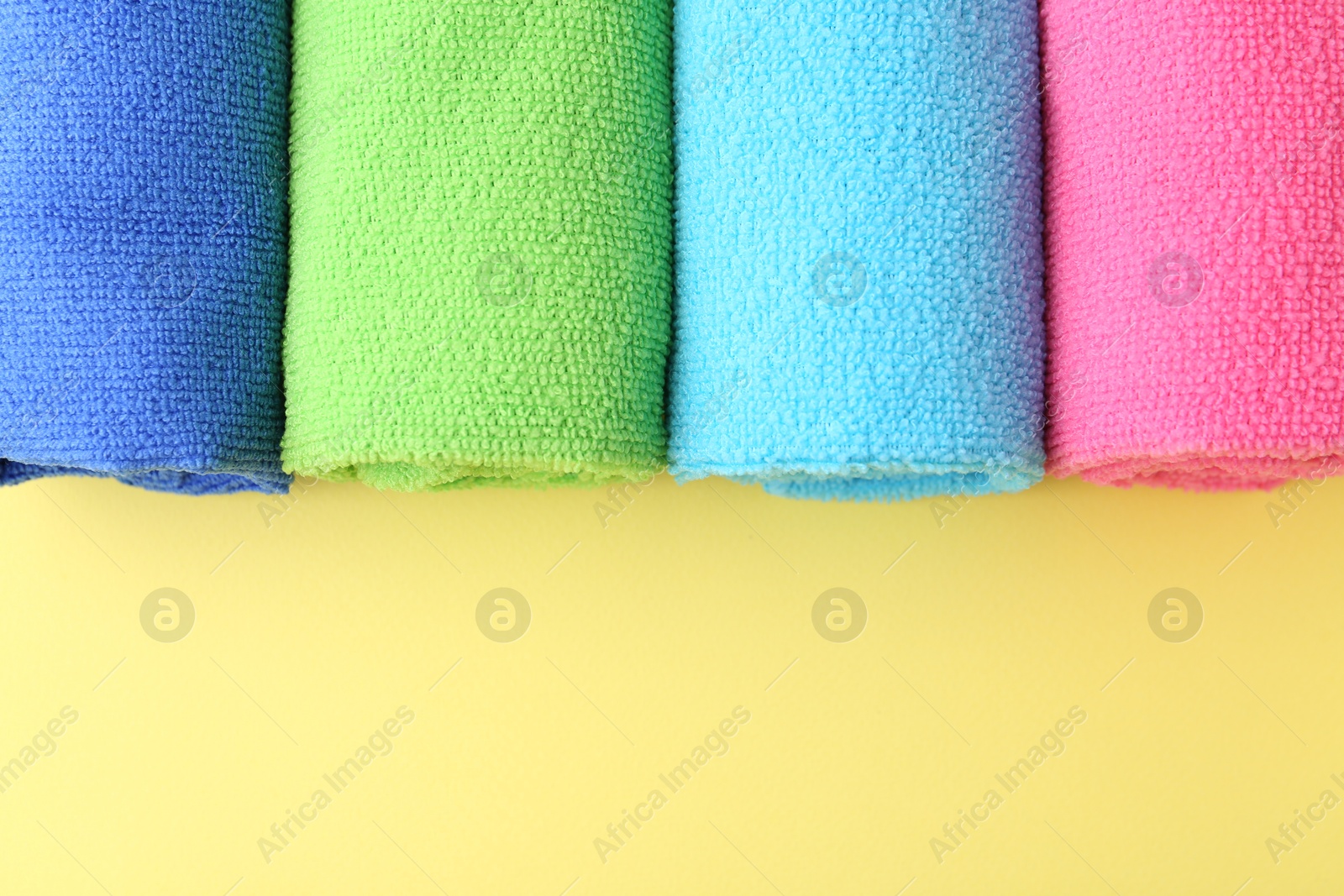 Photo of Rolled different microfiber cloths on yellow background, top view. Space for text