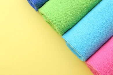 Rolled different microfiber cloths on yellow background, top view. Space for text