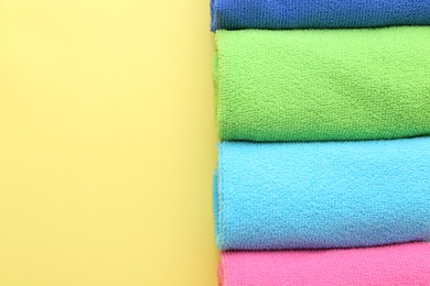 Photo of Rolled different microfiber cloths on yellow background, top view. Space for text