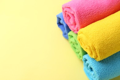 Photo of Rolled different microfiber cloths on yellow background, closeup. Space for text