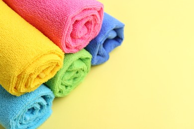 Photo of Rolled different microfiber cloths on yellow background, closeup. Space for text