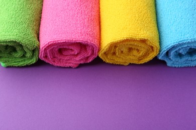 Rolled different microfiber cloths on purple background, closeup. Space for text