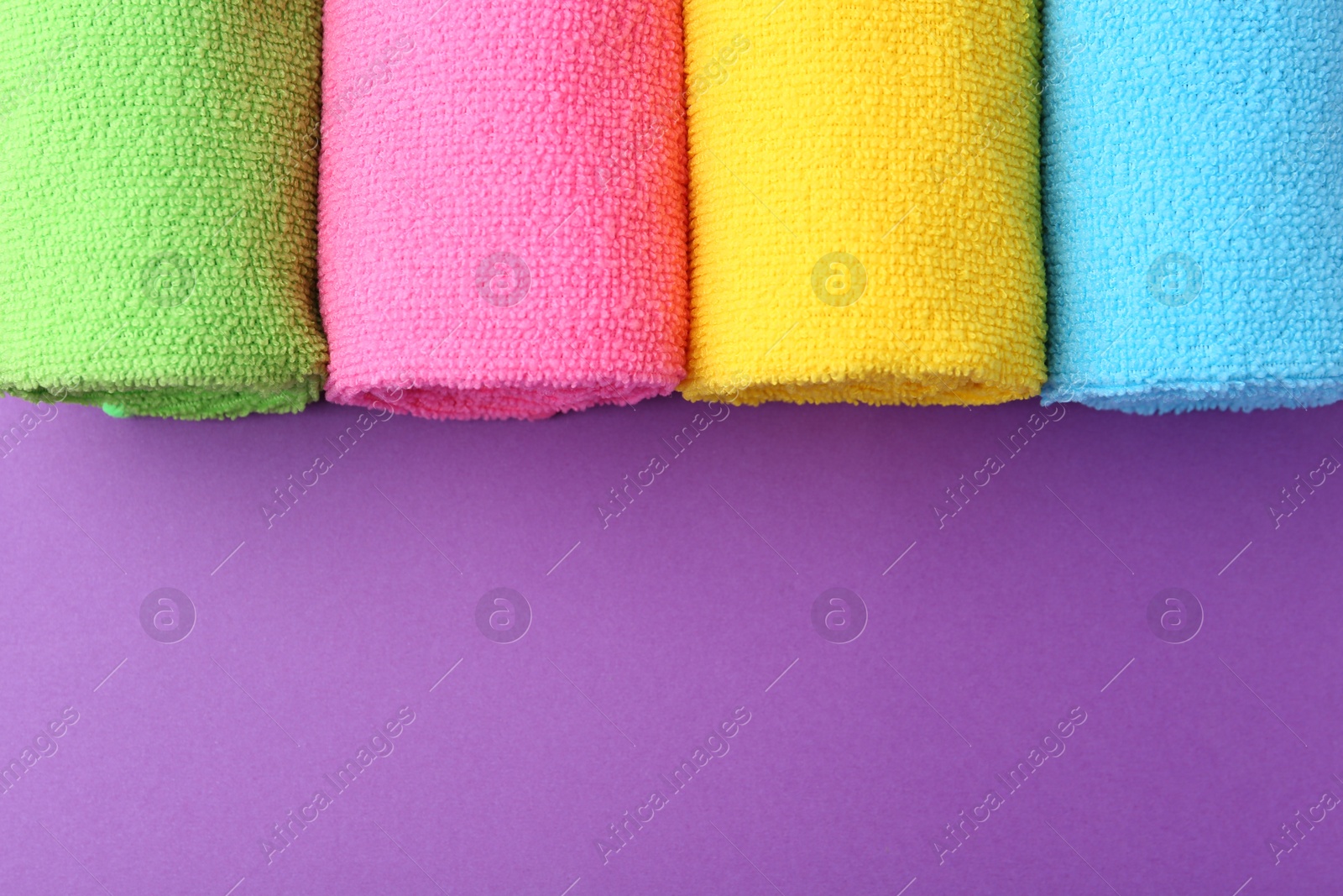 Photo of Rolled different microfiber cloths on purple background, top view. Space for text