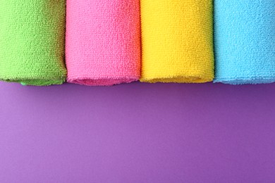 Photo of Rolled different microfiber cloths on purple background, top view. Space for text