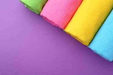 Photo of Rolled different microfiber cloths on purple background, top view. Space for text