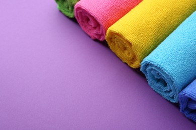 Photo of Rolled different microfiber cloths on purple background, closeup. Space for text