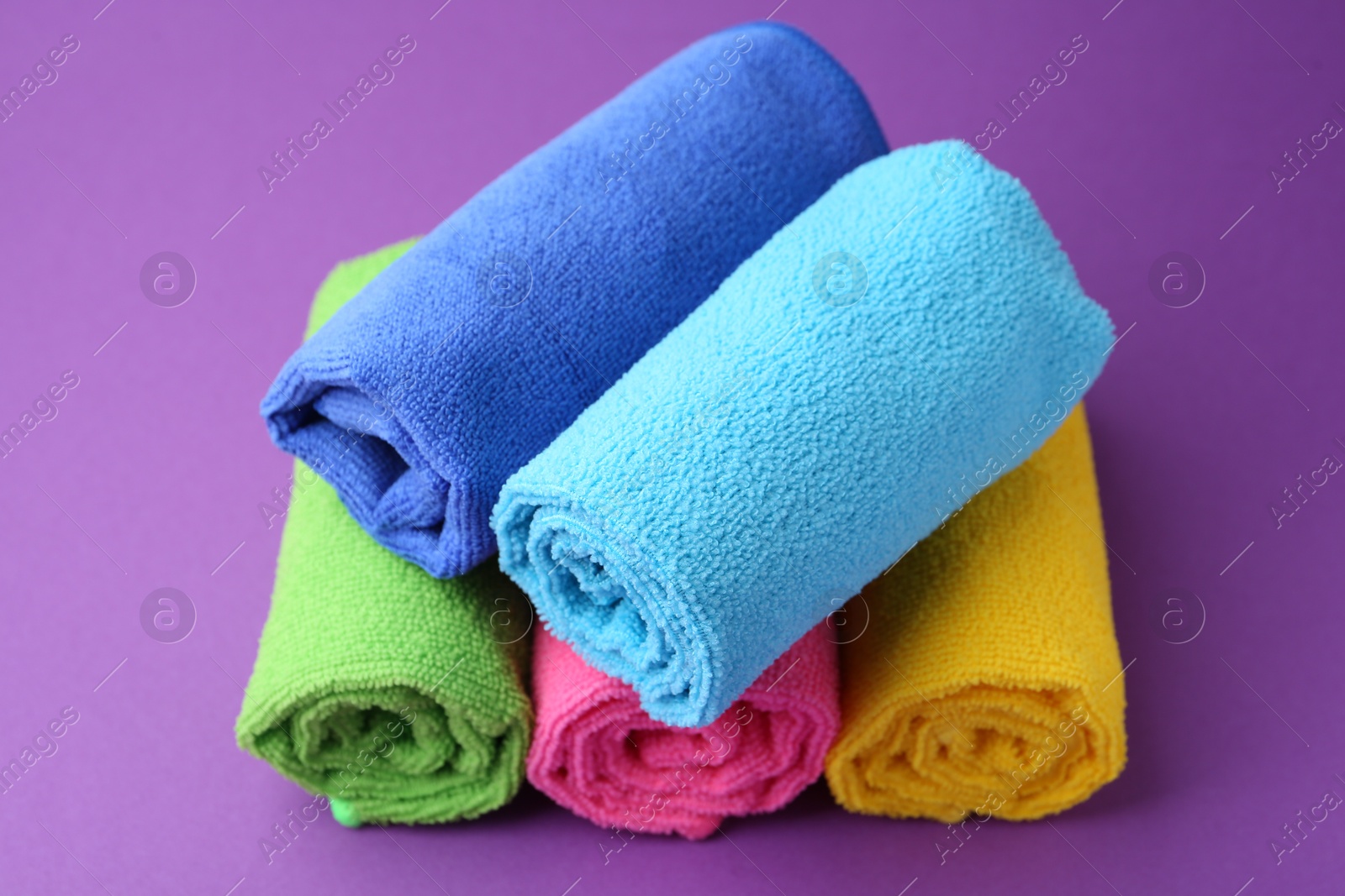 Photo of Rolled different microfiber cloths on purple background, closeup