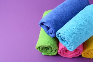 Photo of Rolled different microfiber cloths on purple background, closeup. Space for text