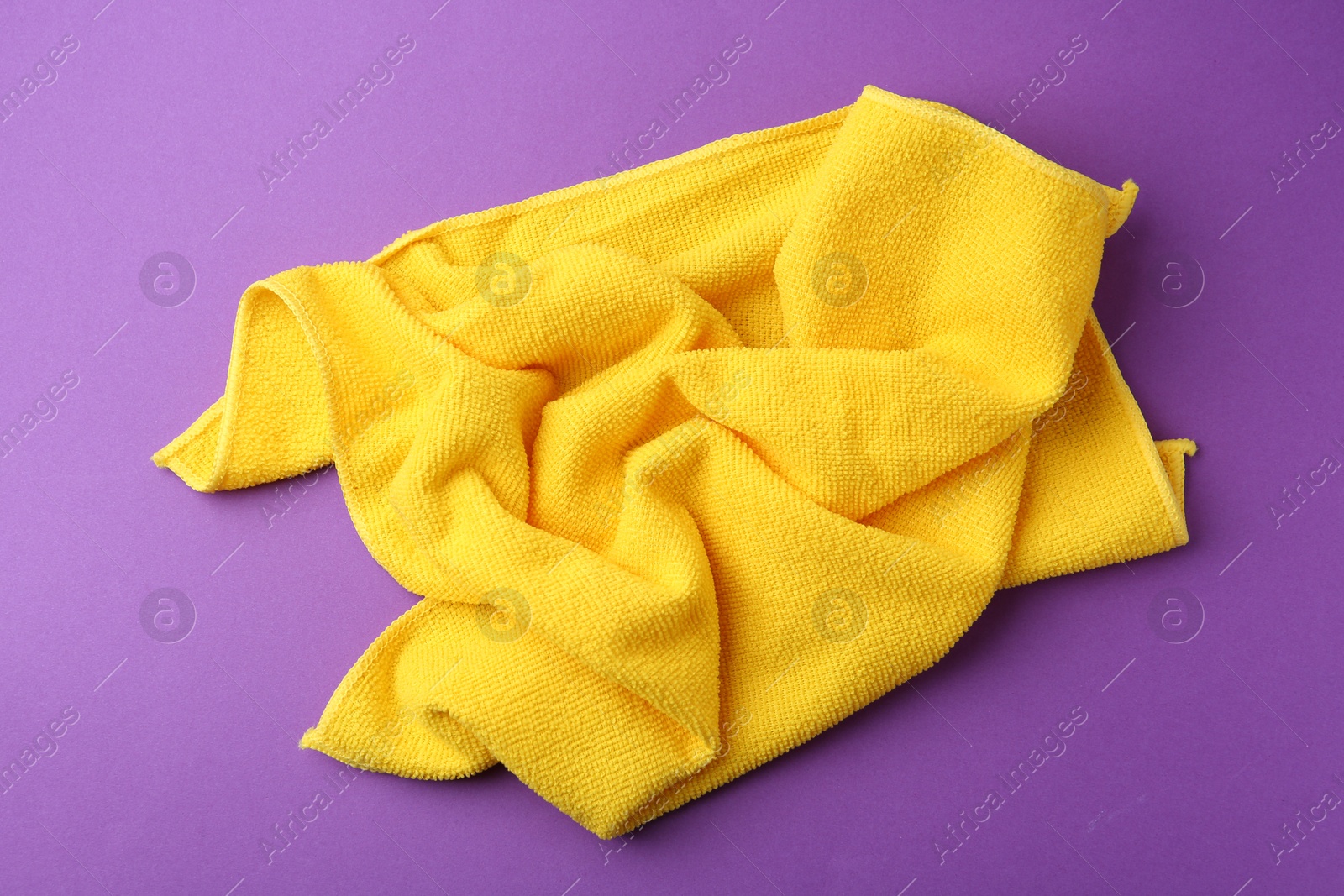 Photo of Clean yellow microfiber cloth on purple background, top view