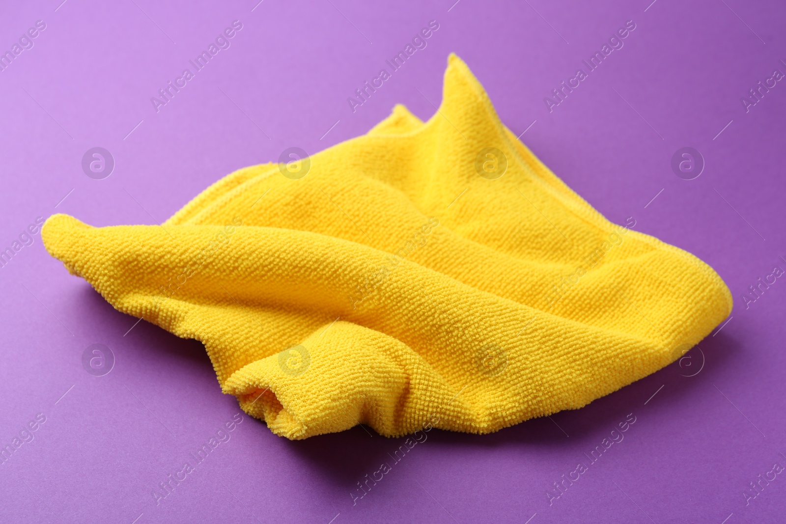 Photo of Clean yellow microfiber cloth on purple background, closeup