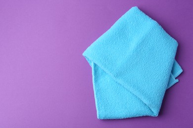 Photo of Clean light blue microfiber cloth on purple background, top view. Space for text