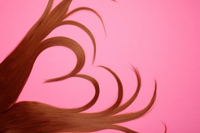 Photo of Red hair strands in shape of heart on pink background, top view. Space for text