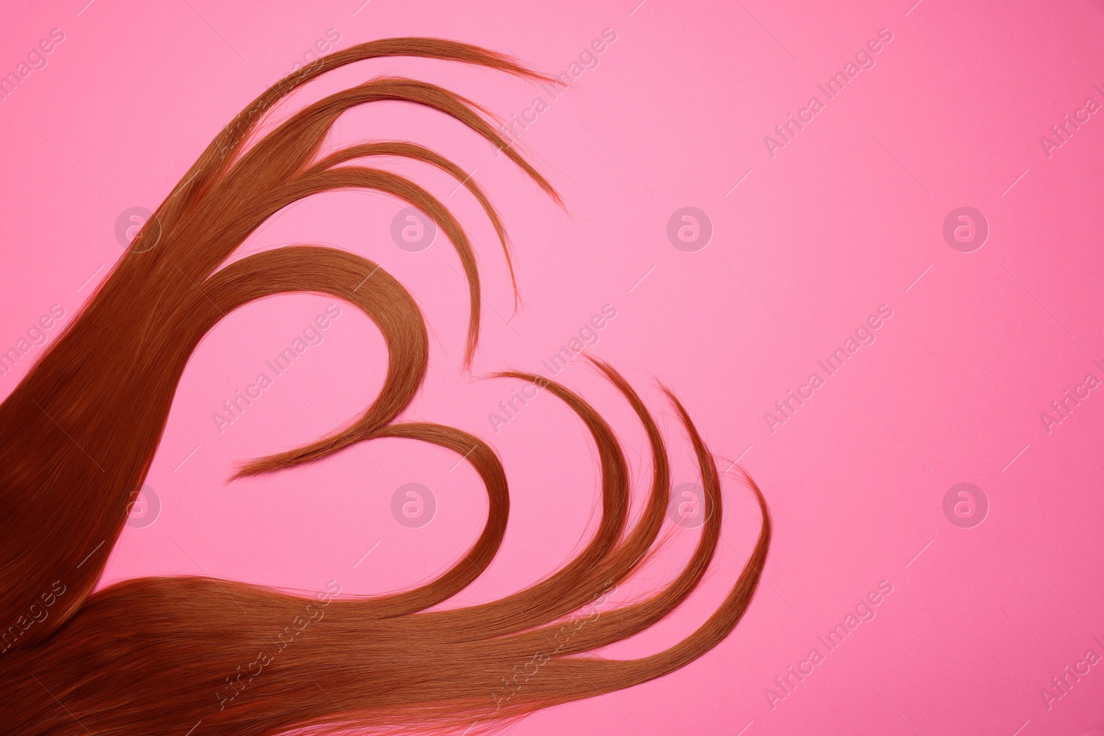 Photo of Red hair strands in shape of heart on pink background, top view. Space for text