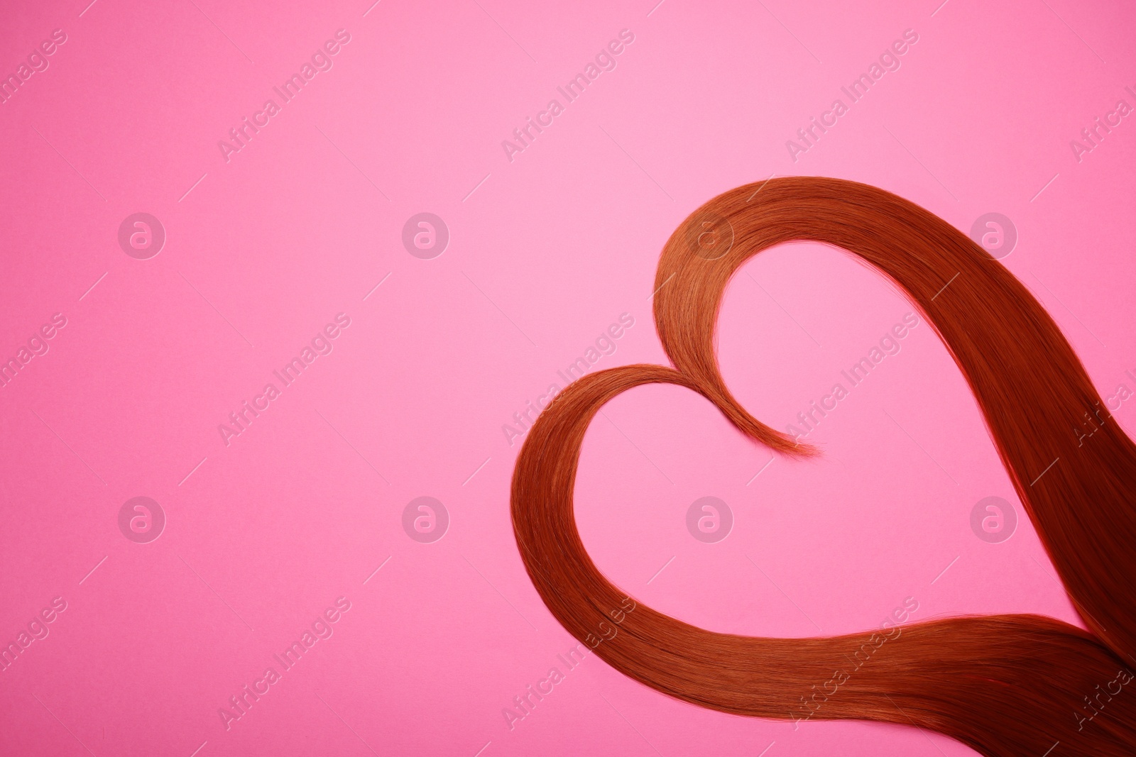 Photo of Red hair strands in shape of heart on pink background, top view. Space for text