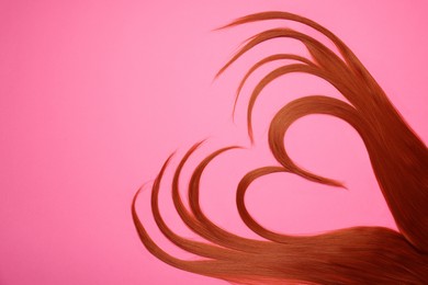 Photo of Red hair strands in shape of heart on pink background, top view. Space for text