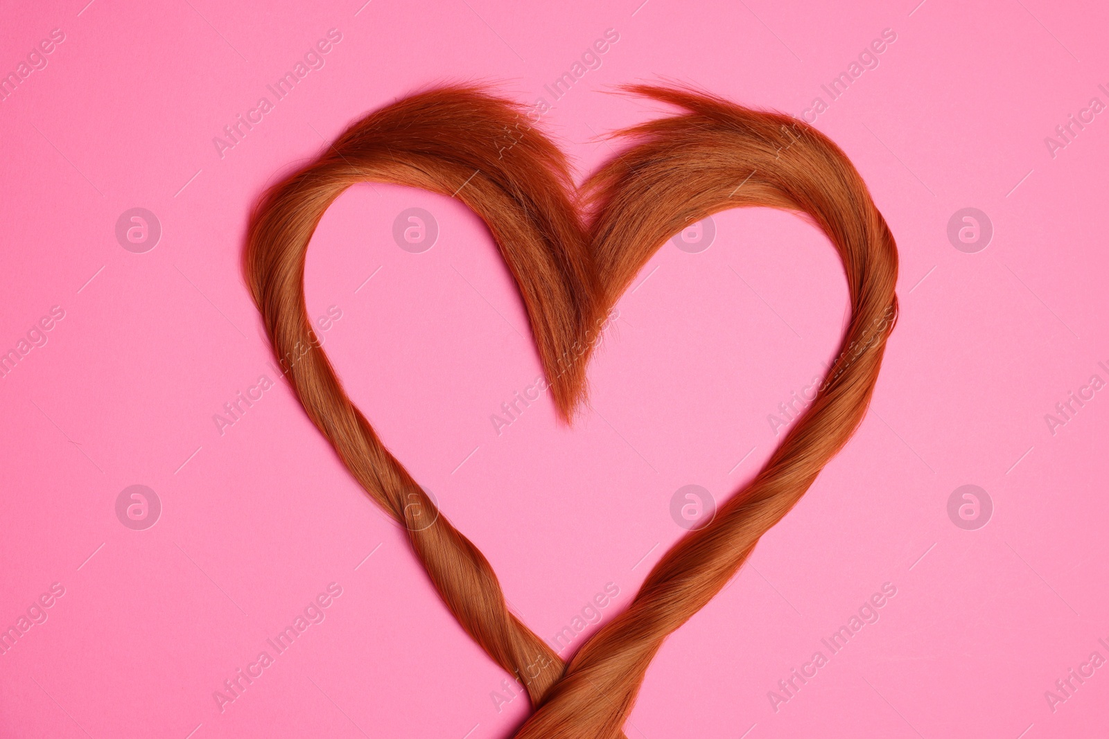 Photo of Red hair strands in shape of heart on pink background, top view