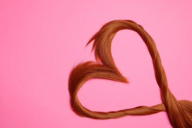 Photo of Red hair strands in shape of heart on pink background, top view. Space for text