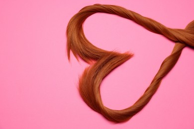 Photo of Red hair strands in shape of heart on pink background, top view. Space for text