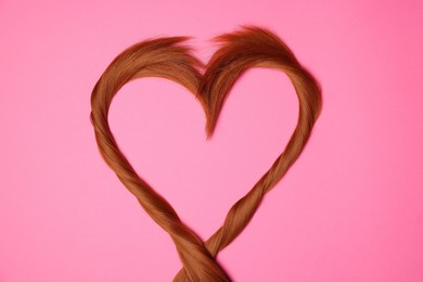 Photo of Red hair strands in shape of heart on pink background, top view