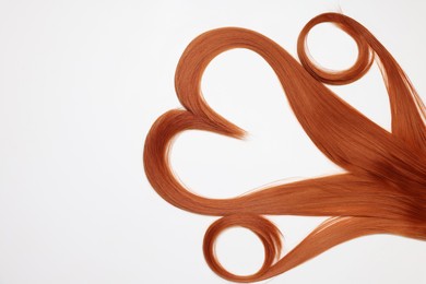 Red hair strands in shape of heart on white background, top view. Space for text