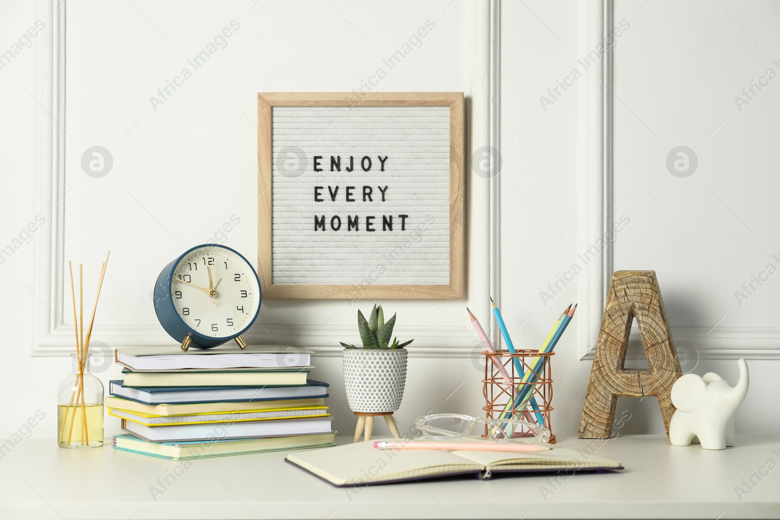 Photo of Letter board with phrase Enjoy Every Moment, alarm clock, decor and stationery on white desk