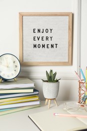 Photo of Letter board with phrase Enjoy Every Moment, alarm clock, decor and stationery on white desk