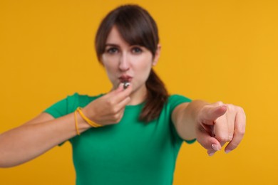 Woman blowing whistle on orange background, selective focus