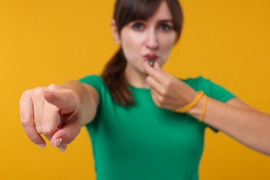 Woman blowing whistle on orange background, selective focus