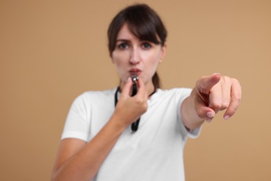 Woman blowing whistle on beige background, selective focus